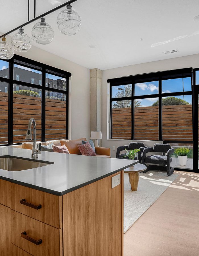 Modern living room with large windows, a kitchen island, and natural light streaming in.