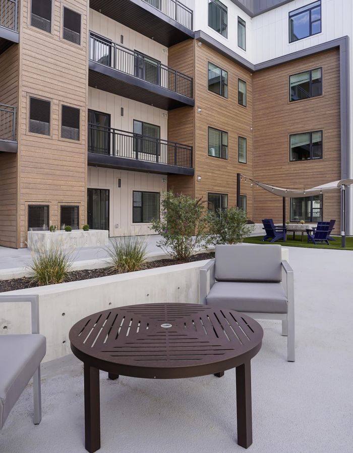 Modern apartment courtyard with outdoor seating, green plants, and shaded lounge areas near building balconies.