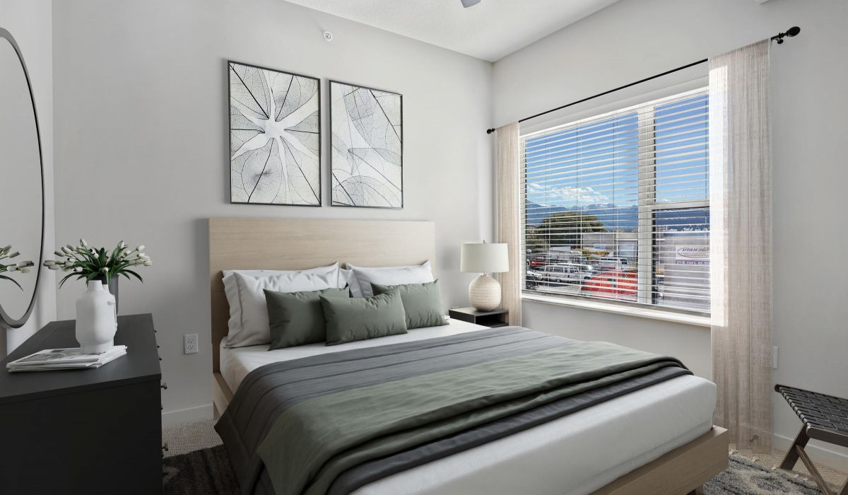 Modern bedroom with a bed, gray bedding, dresser, and large window showing cars and mountains outside.