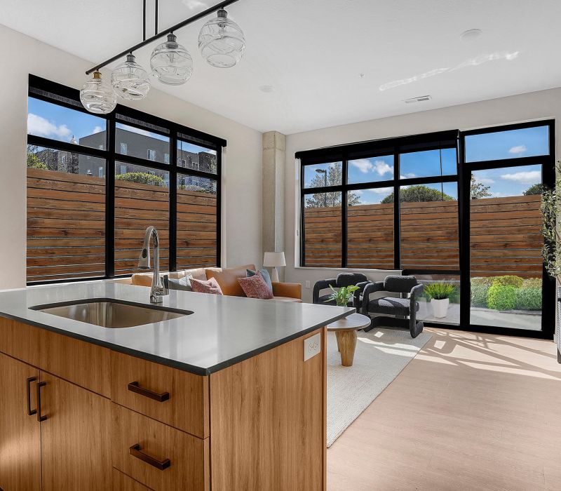 Modern living room with large windows, a kitchen island, and natural light streaming in.