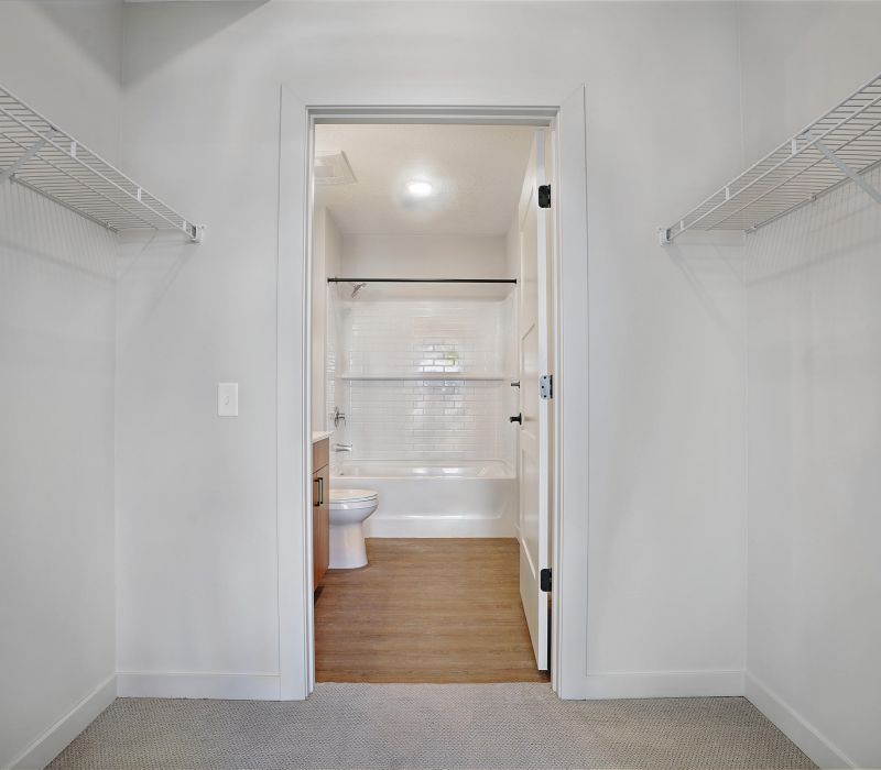 Empty walk-in closet with wire shelves, leading to a bathroom with a toilet, sink, and bathtub.