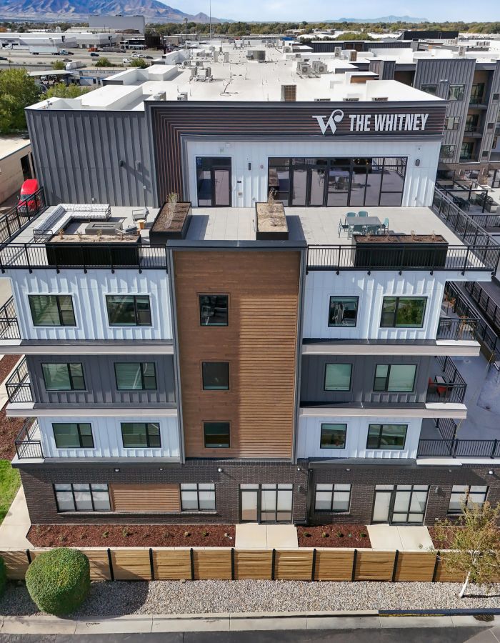 A modern apartment building labeled "The Whitney" with balconies and a rooftop patio.