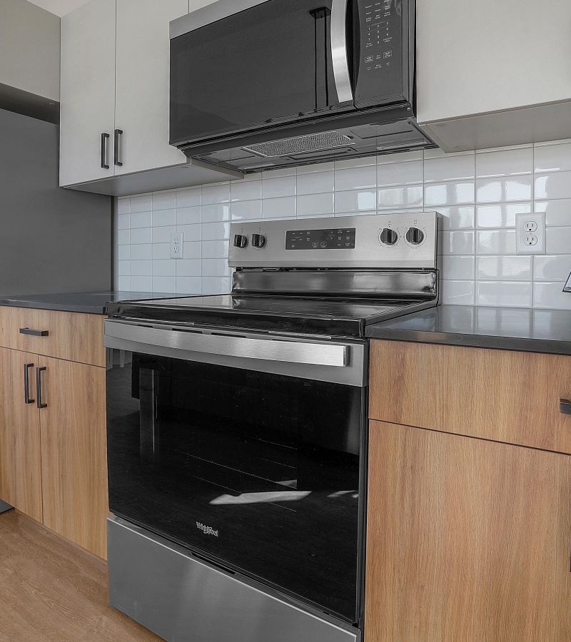 Modern kitchen with stainless steel stove and microwave, white tile backsplash, and wood cabinets.