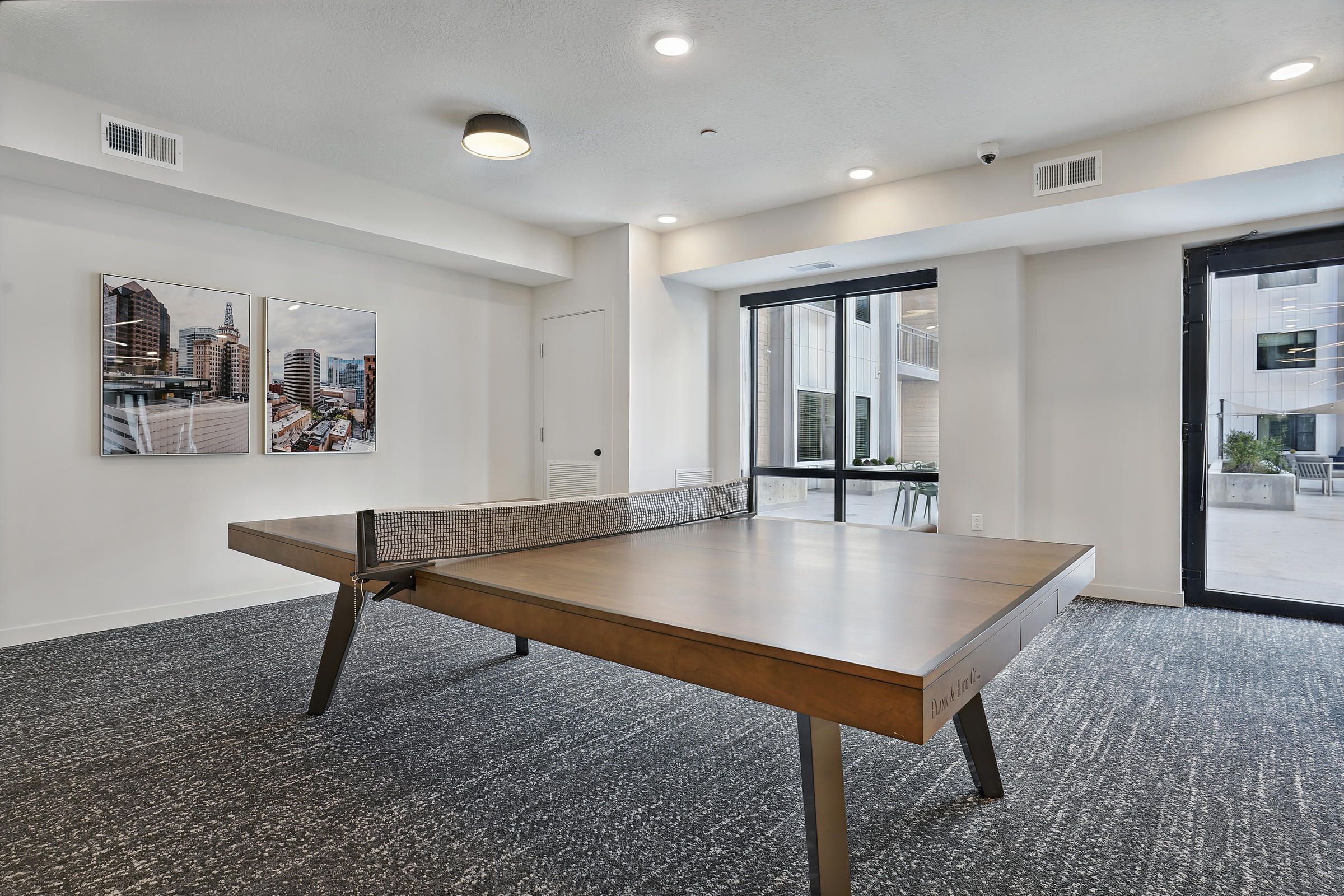 Modern room with a wooden ping pong table, large windows, and cityscape artwork on the wall.